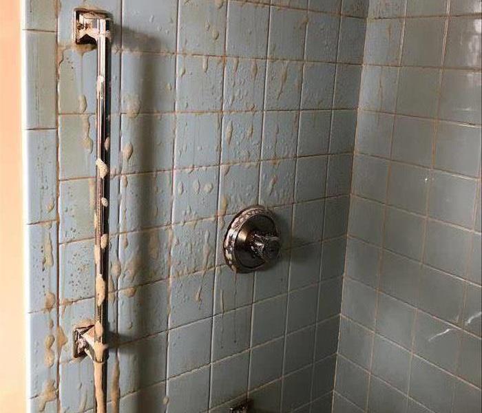 a blue tiled shower with blue tiles covered in suds and orange grime