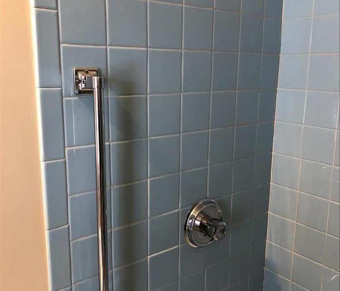 a blue tile shower with white grout lines and shiny metal handles
