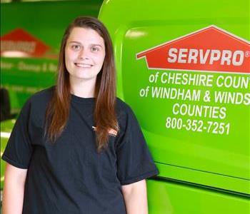 Young female SERVPRO employee with long dark hair wearing a SERVPRO sweatshirt standing in front of a SERVPRO van