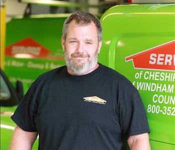 Male SERVPRO employee with mustache and short hair wearing a SERVPRO Tee Shirt and standing in front of a SERVPRO van