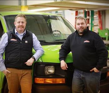 Two men standing in front of a green SERVPRO van
