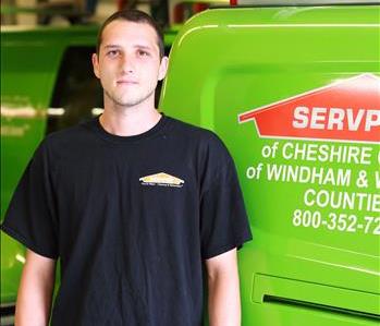 Young male SERVPRO employee wearing a black SERVPRO Tee Shirt over gray long sleeved shirt standing in front of a SERVPRO van