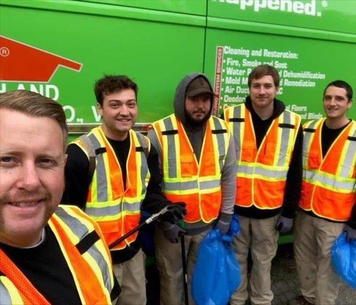 SERVPRO employees wearing visibility vests and standing outside in front of a SERVPRO van