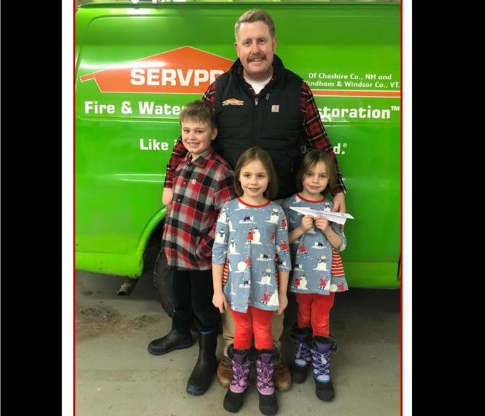 a man and three children (a boy and twin girls) stand in front of a green SERVPRO van
