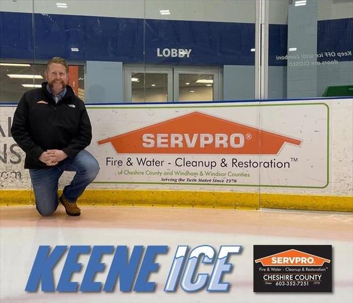Man kneeling on ice in front of SERVPRO sign on hockey boards.