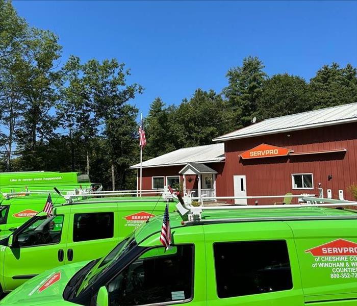 Row of green trucks in front of large red commercial building.