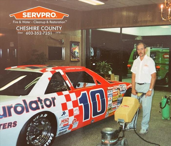 Man shampooing carpets in an office next to a race car.