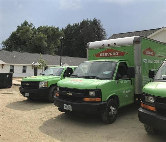 Three green SERVPRO trucks parked outside commercial property.